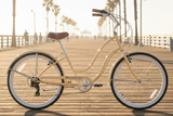 Lifestyle photography of a Vanilla Firmstrong Siren Women's beach cruiser bicycle parked on a sunny ocean pier with palm trees